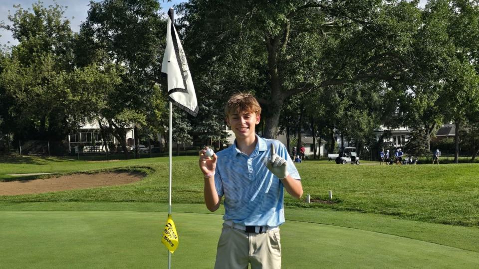 Golfer standing by a golf hole, holding a golf ball. 